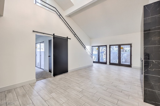 empty room featuring a barn door, french doors, high vaulted ceiling, and light hardwood / wood-style floors