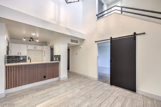 kitchen with light wood-type flooring, a towering ceiling, tasteful backsplash, a barn door, and white cabinetry