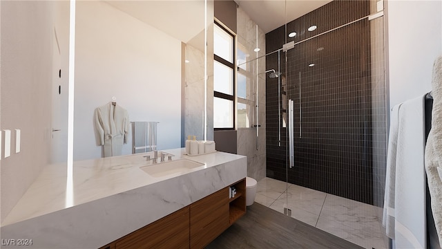 bathroom with toilet, vanity, a tile shower, and wood-type flooring