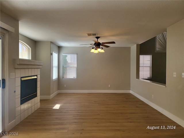 unfurnished living room with wood-type flooring, a tile fireplace, and ceiling fan