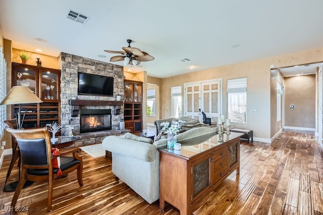 living room with hardwood / wood-style floors, a stone fireplace, and ceiling fan