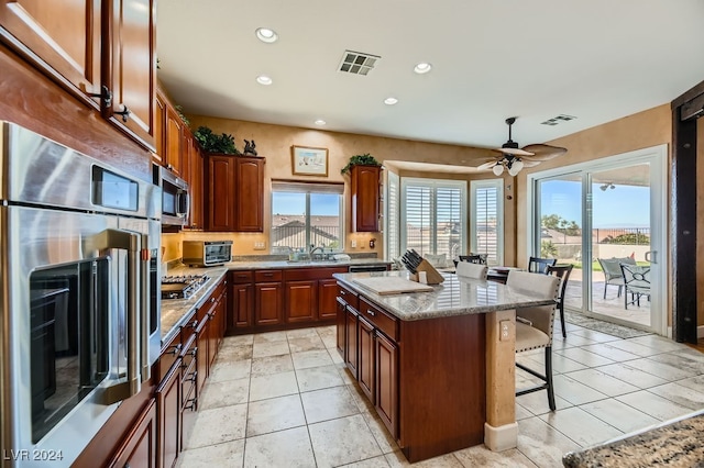 kitchen featuring appliances with stainless steel finishes, a breakfast bar, ceiling fan, light tile patterned floors, and a kitchen island