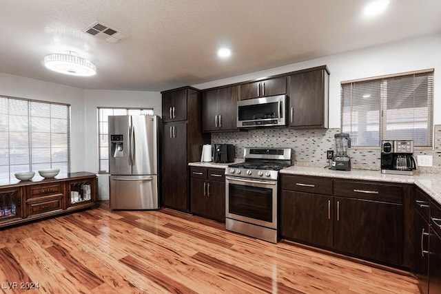 kitchen featuring light wood-type flooring, tasteful backsplash, light stone counters, dark brown cabinetry, and stainless steel appliances