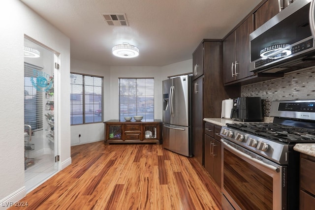 kitchen featuring light hardwood / wood-style flooring, light stone countertops, appliances with stainless steel finishes, tasteful backsplash, and dark brown cabinetry