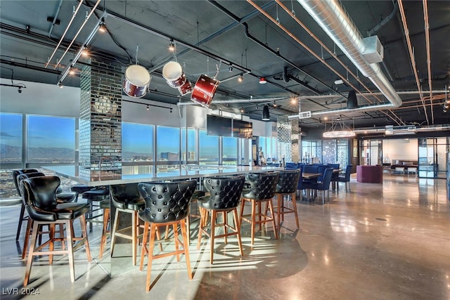 dining area with concrete floors, a water view, decorative columns, and bar area