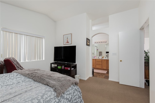 bedroom with ensuite bath, light colored carpet, and vaulted ceiling