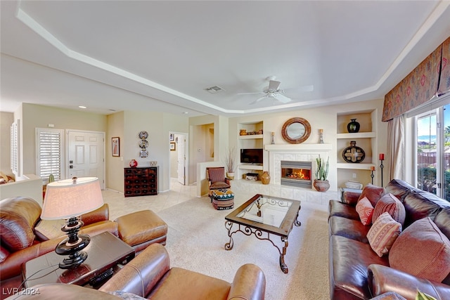 carpeted living room featuring ceiling fan, a tray ceiling, a tile fireplace, and built in features