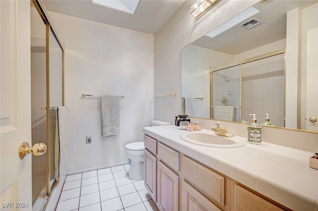 bathroom with tile patterned floors, a shower with door, vanity, toilet, and a skylight