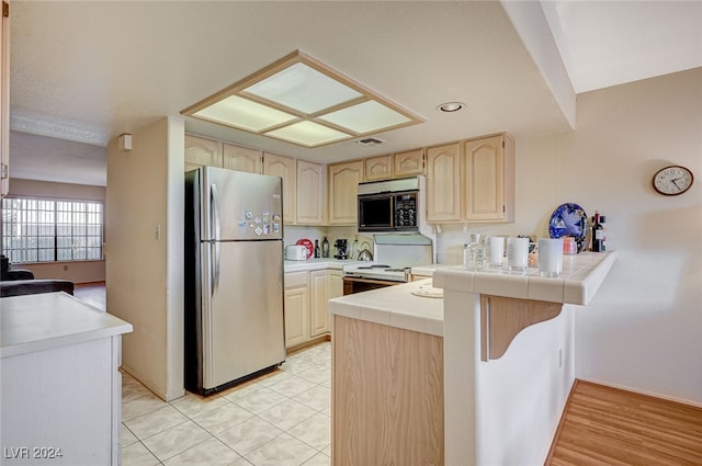 kitchen with tile counters, kitchen peninsula, stainless steel fridge, light hardwood / wood-style floors, and electric stove