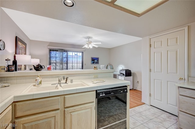 kitchen featuring tile countertops, sink, light tile patterned floors, black dishwasher, and ceiling fan