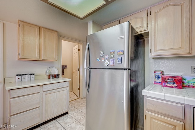 kitchen featuring tile countertops, stainless steel fridge, light brown cabinetry, and light tile patterned floors