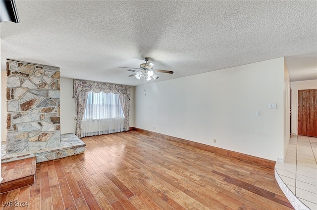 unfurnished living room featuring a textured ceiling, light wood-type flooring, and ceiling fan