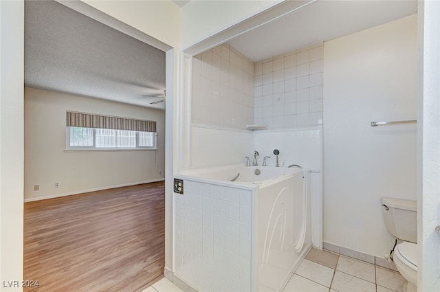 bathroom featuring hardwood / wood-style flooring, toilet, a tub, a textured ceiling, and ceiling fan