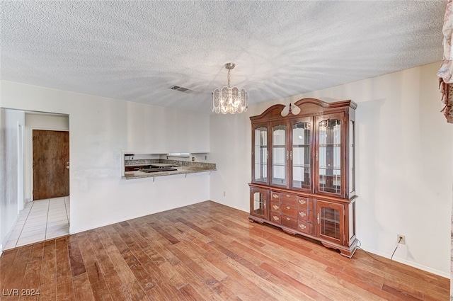 unfurnished dining area featuring an inviting chandelier, a textured ceiling, and light wood-type flooring