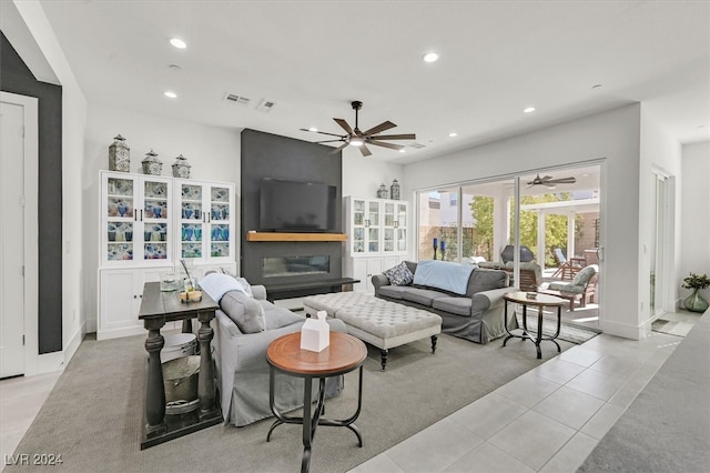 tiled living room featuring ceiling fan and a large fireplace