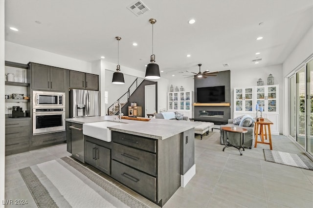 kitchen featuring sink, a center island with sink, appliances with stainless steel finishes, decorative light fixtures, and ceiling fan