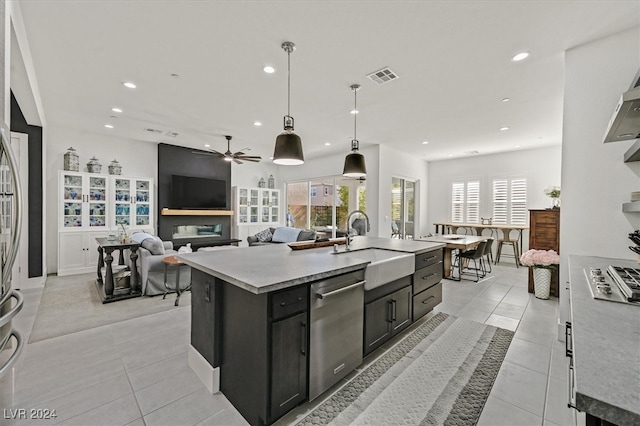 kitchen with sink, hanging light fixtures, light tile patterned floors, a kitchen island with sink, and stainless steel dishwasher