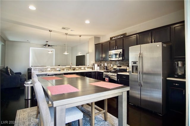 kitchen featuring ceiling fan, decorative backsplash, decorative light fixtures, kitchen peninsula, and stainless steel appliances