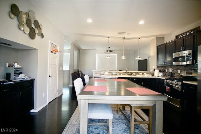 kitchen with decorative backsplash, stainless steel appliances, ceiling fan, dark wood-type flooring, and hanging light fixtures