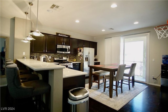 kitchen with kitchen peninsula, appliances with stainless steel finishes, dark wood-type flooring, pendant lighting, and a breakfast bar area