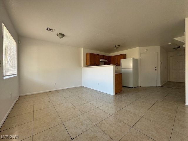 interior space featuring kitchen peninsula, white fridge, and light tile patterned flooring