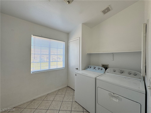 laundry area featuring separate washer and dryer, light tile patterned floors, and a textured ceiling