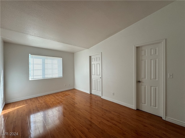 empty room featuring a textured ceiling, hardwood / wood-style flooring, and lofted ceiling