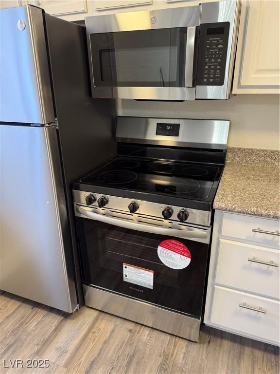 5317 Indian River Dr Unit 295, Las Vegas, NV 89103 - kitchen with appliances with stainless steel finishes, light wood-type flooring, white cabinetry, and light stone countertops