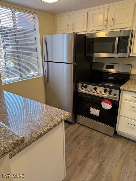 5317 Indian River Dr Unit 295, Las Vegas, NV 89103 - kitchen featuring appliances with stainless steel finishes, light wood-style floors, white cabinets, and dark stone countertops