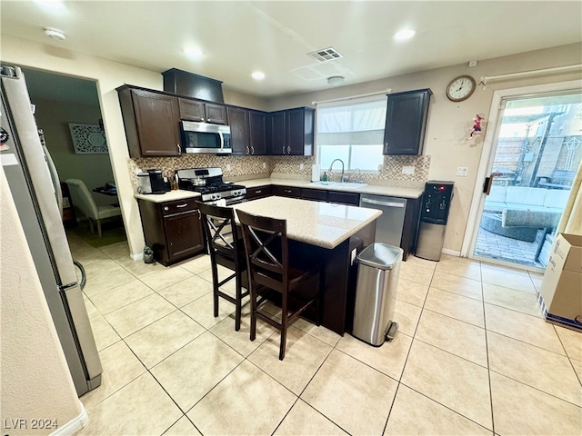 kitchen with sink, appliances with stainless steel finishes, dark brown cabinets, a kitchen island, and a kitchen bar