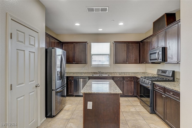 kitchen with light stone countertops, stainless steel appliances, a kitchen island, dark brown cabinets, and light tile patterned flooring