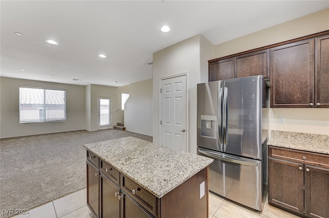 kitchen featuring light stone countertops, stainless steel fridge, a center island, and light colored carpet