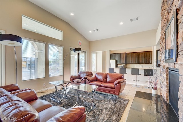 living room featuring light tile patterned flooring, a stone fireplace, and high vaulted ceiling