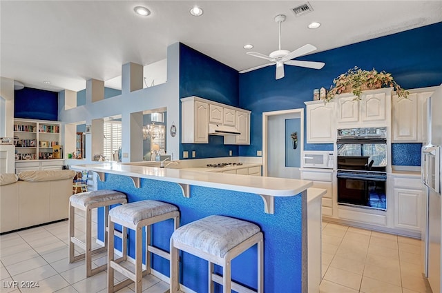 kitchen with a breakfast bar area, kitchen peninsula, light tile patterned floors, and white appliances