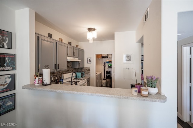 kitchen with washer and clothes dryer, gray cabinets, tasteful backsplash, kitchen peninsula, and white range with gas cooktop