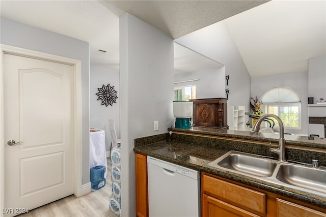 kitchen featuring sink, white dishwasher, dark stone counters, vaulted ceiling, and light wood-type flooring