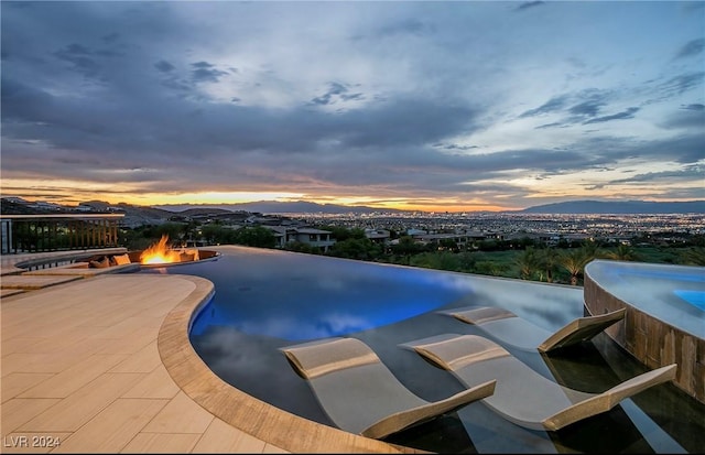 pool at dusk featuring a mountain view, a patio area, and an outdoor fire pit