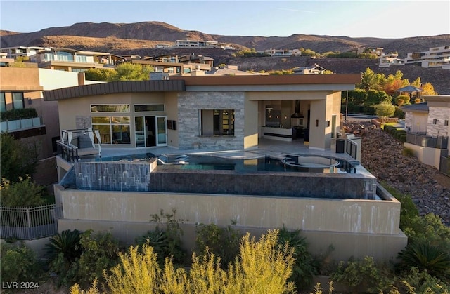 back of property featuring an in ground hot tub, a mountain view, and a patio area