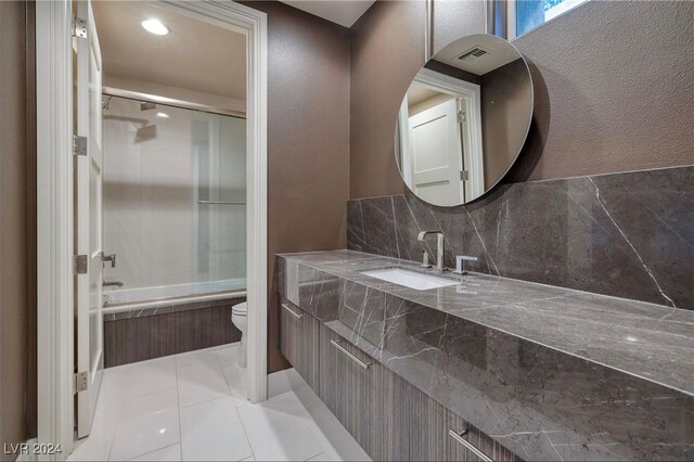 full bathroom with toilet, combined bath / shower with glass door, vanity, tile patterned flooring, and backsplash