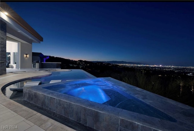 pool at dusk with an in ground hot tub and a patio area