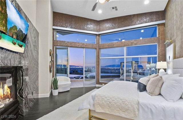 bedroom featuring hardwood / wood-style flooring, a towering ceiling, and a high end fireplace