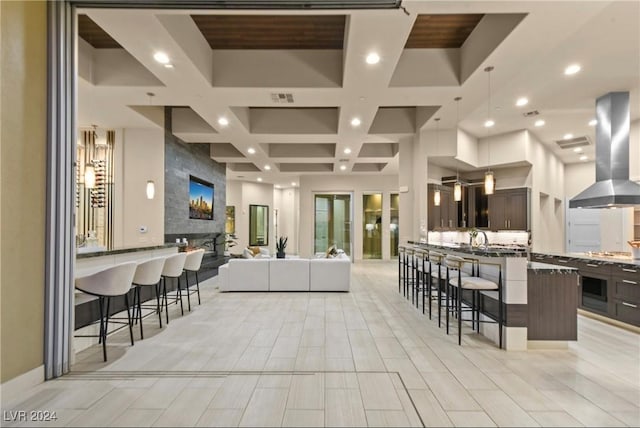 kitchen featuring island range hood, a breakfast bar, dark brown cabinets, and a center island with sink