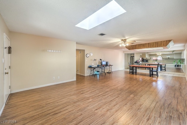 recreation room featuring ceiling fan, light wood-type flooring, a textured ceiling, and a skylight