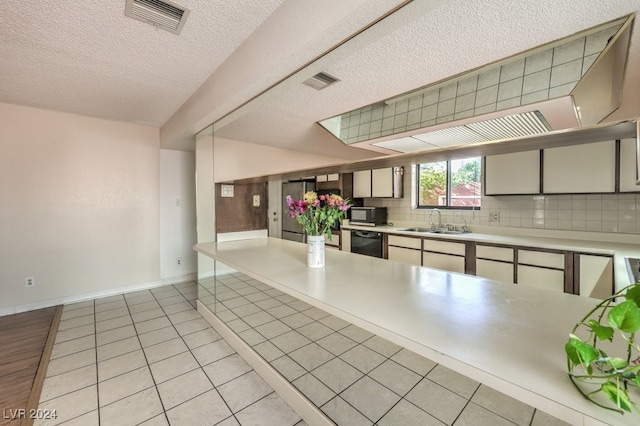 kitchen with tasteful backsplash, a textured ceiling, sink, light tile patterned floors, and dishwasher