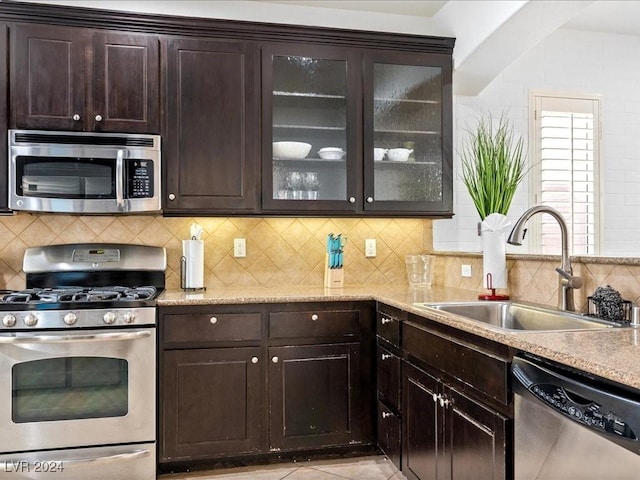 kitchen featuring decorative backsplash, a sink, stainless steel appliances, dark brown cabinetry, and glass insert cabinets