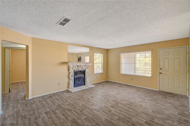 unfurnished living room featuring a stone fireplace, hardwood / wood-style floors, and a textured ceiling