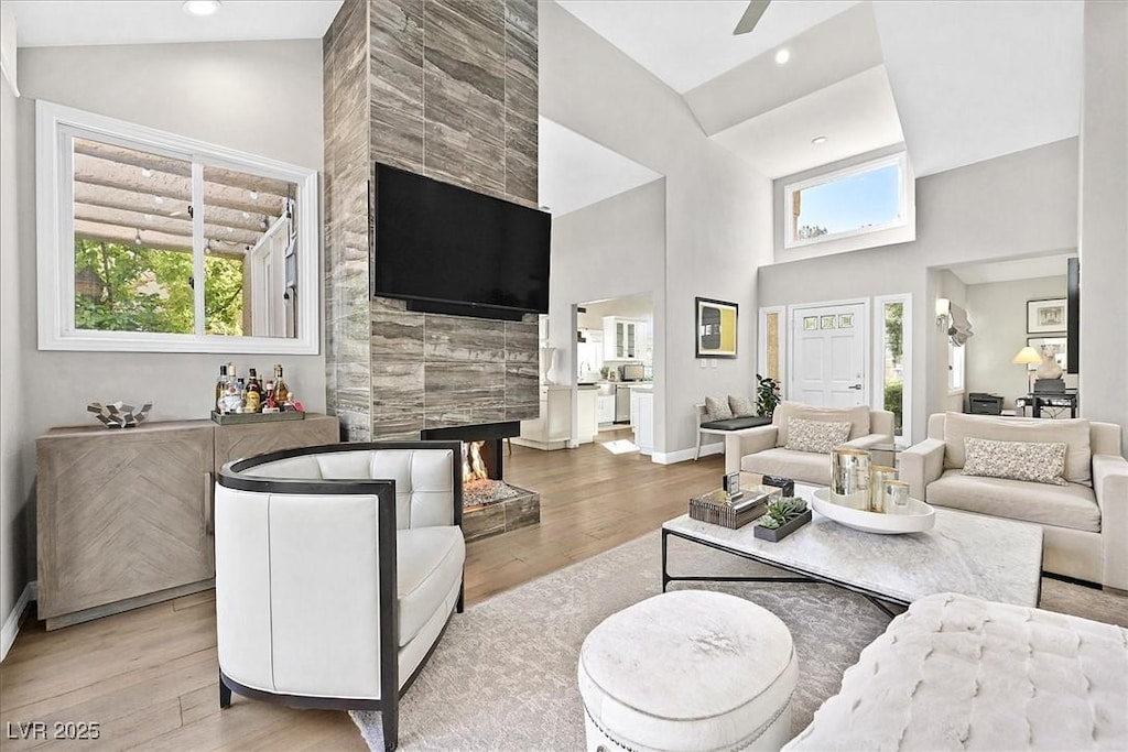 living room with a tile fireplace, light wood-type flooring, high vaulted ceiling, and ceiling fan