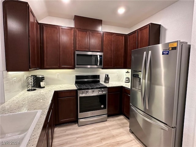 kitchen with light stone counters, tasteful backsplash, appliances with stainless steel finishes, light wood-style floors, and a sink