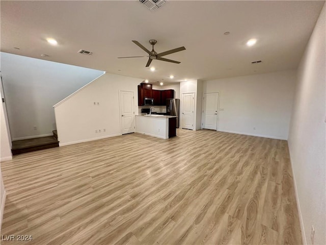 unfurnished living room featuring baseboards, visible vents, a ceiling fan, light wood-style floors, and a sink