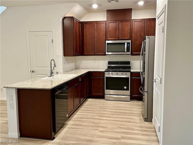 kitchen featuring light stone countertops, light wood-style flooring, stainless steel appliances, and a sink